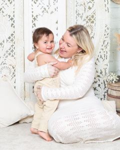 A little boy smiles for the camera as he's getting a big hug from his mum