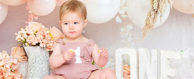 A little girl looks disappovingly off camera at her cake smash photo shoot