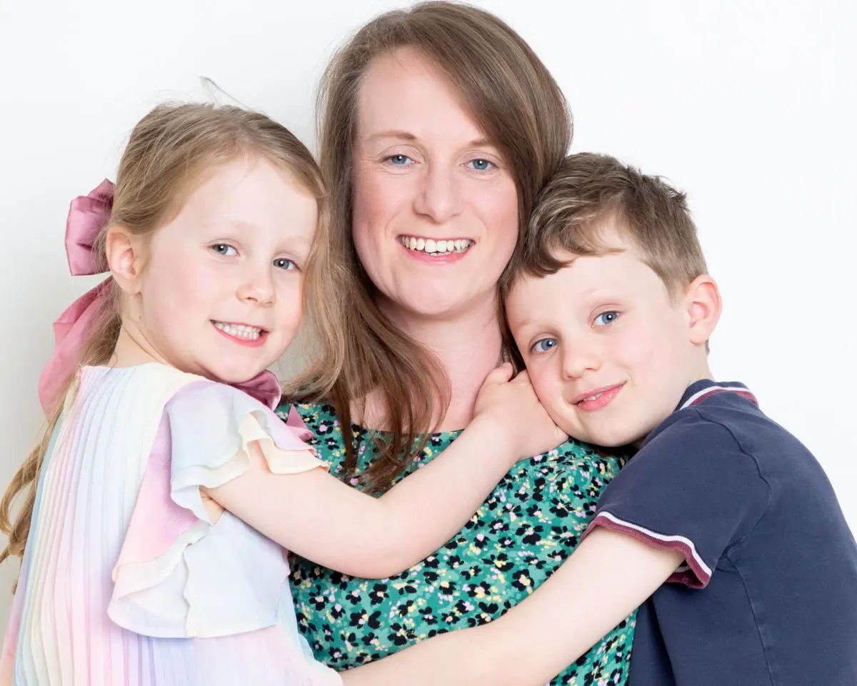 A mother smiles for the camera while holding both her children