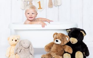 a little boy in a bathtub with teddy bears sitting beside him