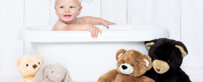a little boy in a bathtub with teddy bears sitting beside him