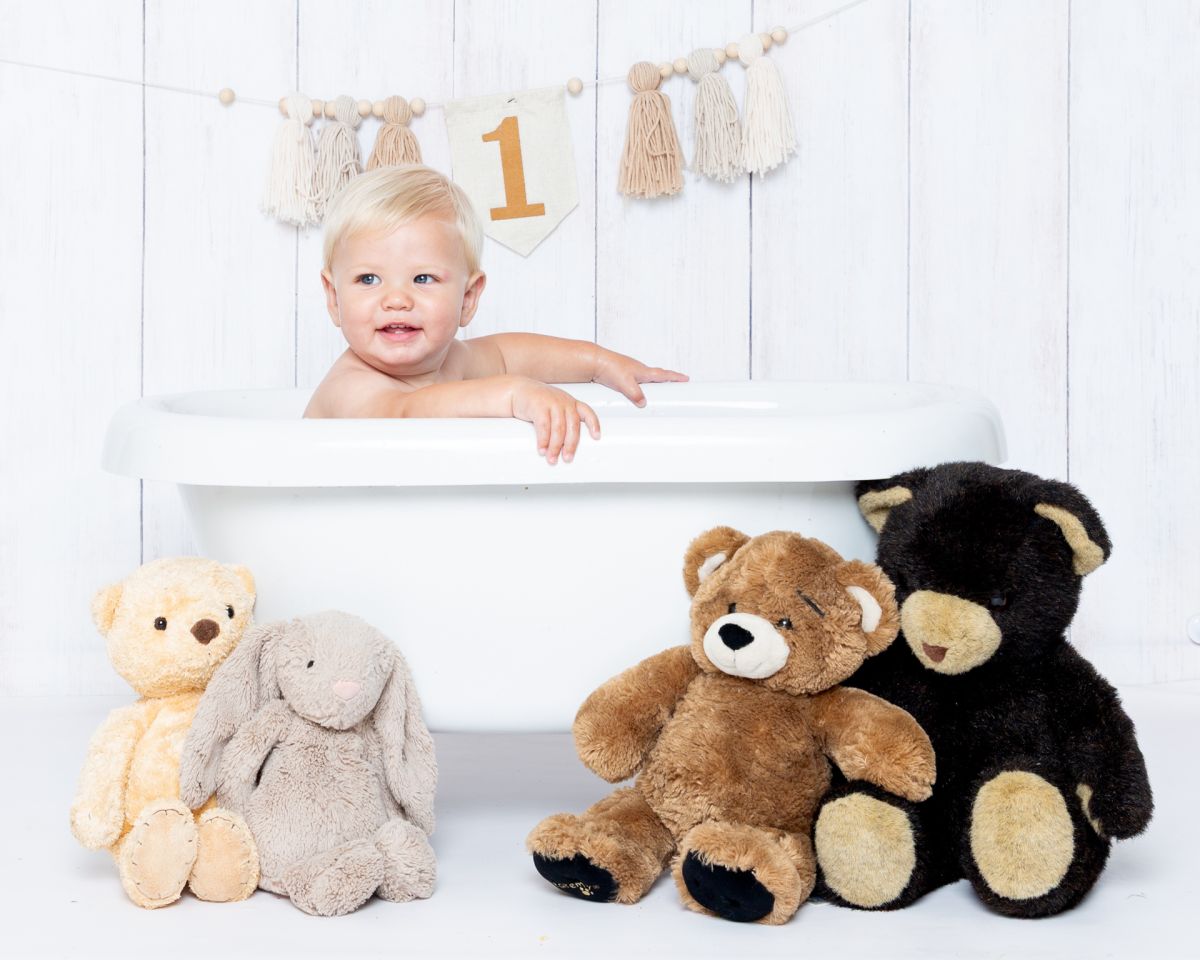 a little boy in a bathtub with teddy bears sitting beside him
