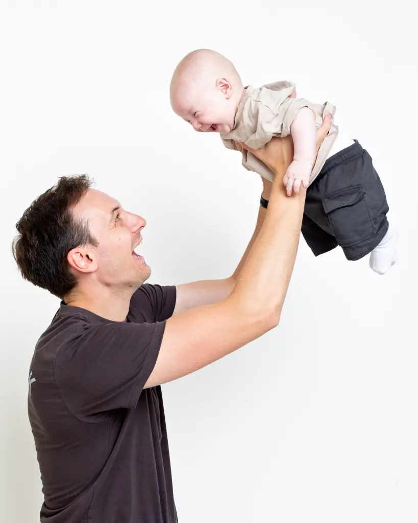 A dad flies his little boy up into the air and he's laughing