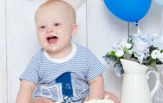 A little boy sits behind a cake with blue balloons and bunting
