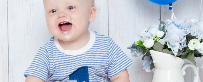 A little boy sits behind a cake with blue balloons and bunting