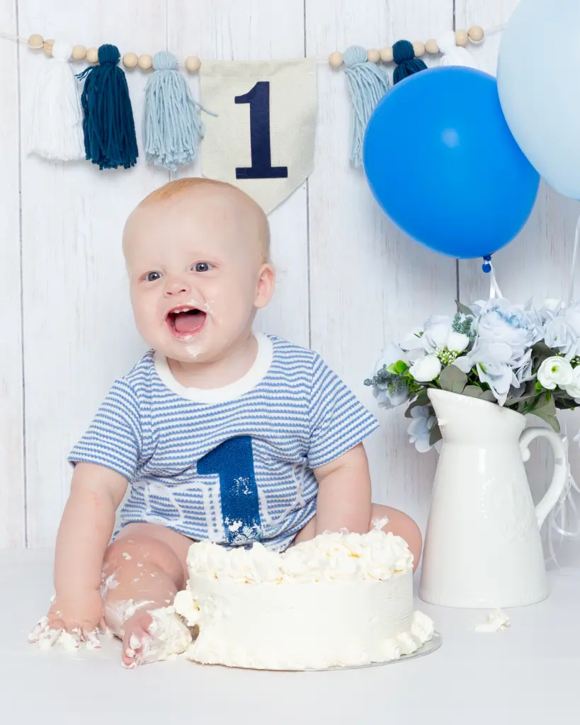 First Birthday Photo Shoot West Sussex A little boy sits behind a cake with blue balloons and bunting