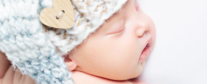 A sleeping newborn in close up wearing a long tail hat