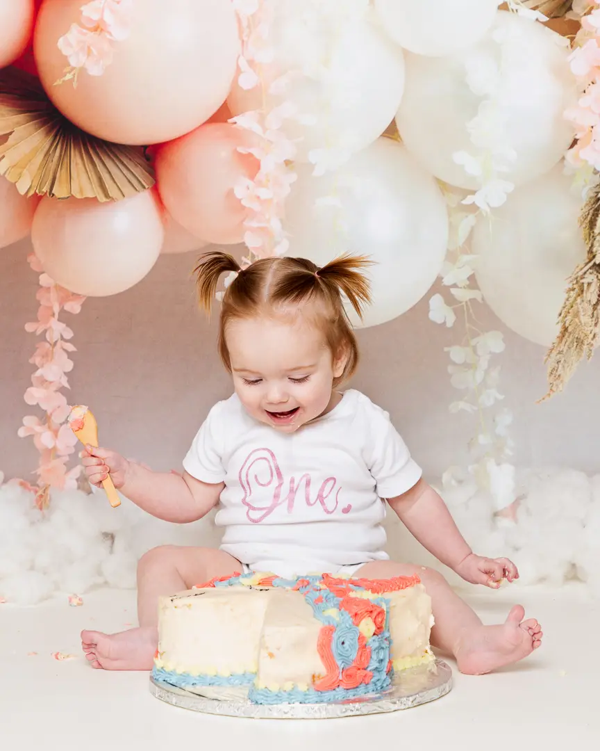 A little girl smashes her unicorn cake at a first birthday photo shoot