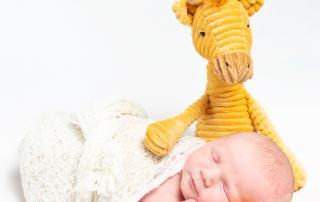 a newborn sleeps with their head on the legs of their first toy as a pillow