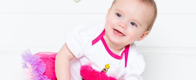 a little girl poses by her cake in a pink pettiskirt with pink tassels behind her - West Sussex