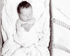 a black and white image of a newborn swaddled and sleeping in a moses basket
