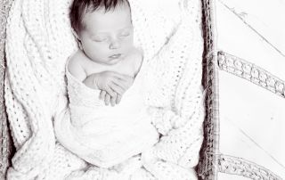 a black and white image of a newborn swaddled and sleeping in a moses basket