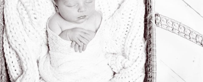 a black and white image of a newborn swaddled and sleeping in a moses basket