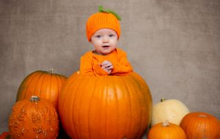 a baby in a pumpkin hat, sitting in a giant pumpkin