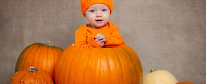 a baby in a pumpkin hat, sitting in a giant pumpkin