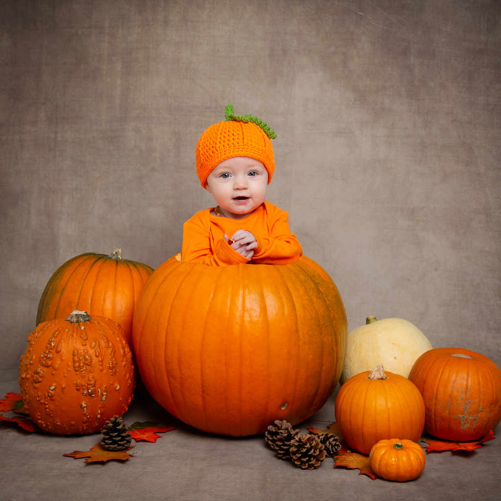 a baby in a pumpkin hat, sitting in a giant pumpkin