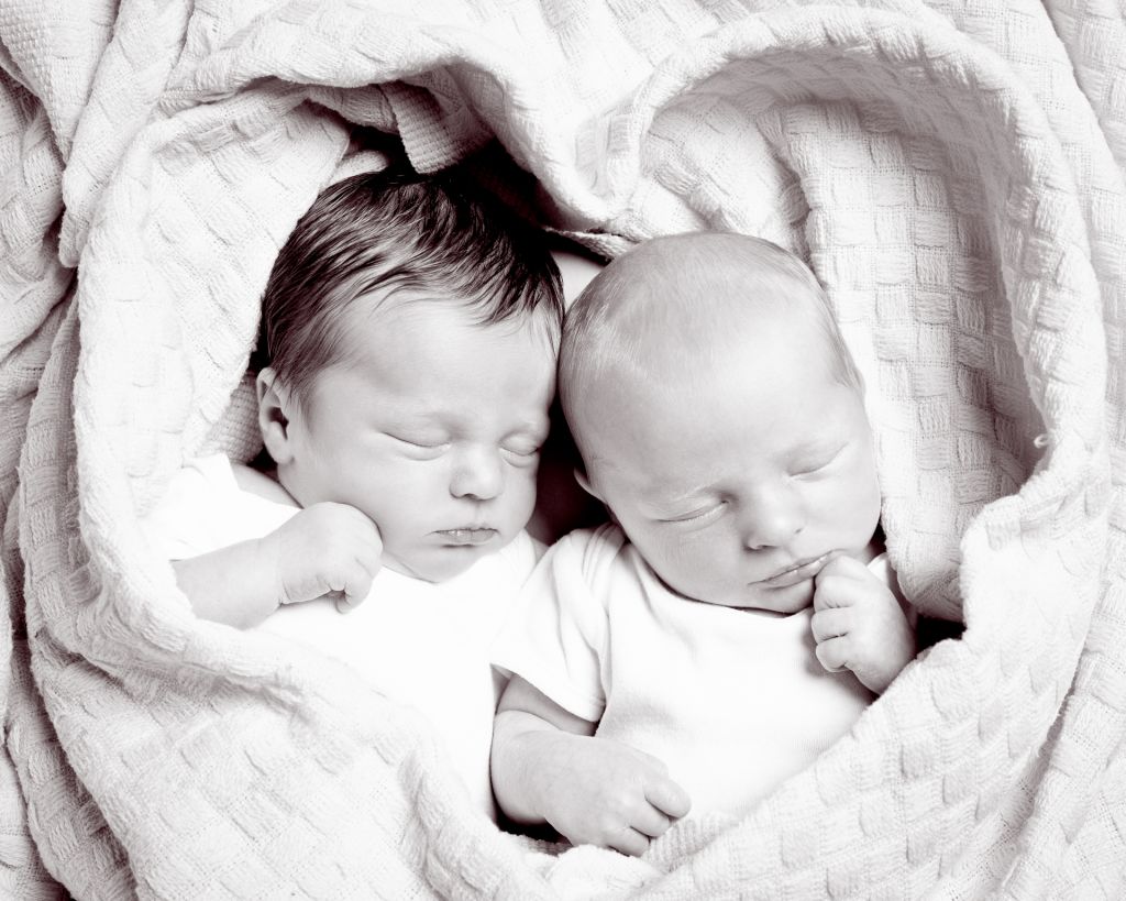 A black and white image of newborn twins wrapped in a blanket shaped like a heartr