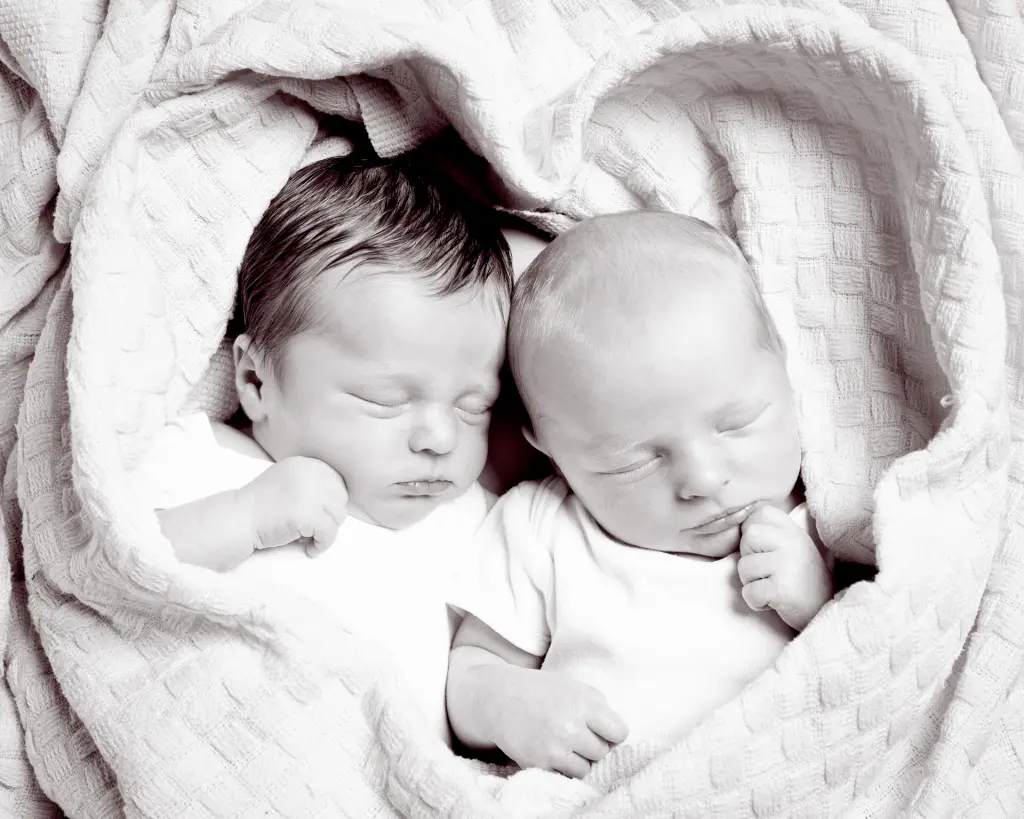 A black and white image of newborn twins wrapped in a blanket shaped like a heartr
