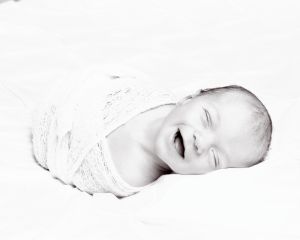 A black and white image of a smiling newborn swaddled in white