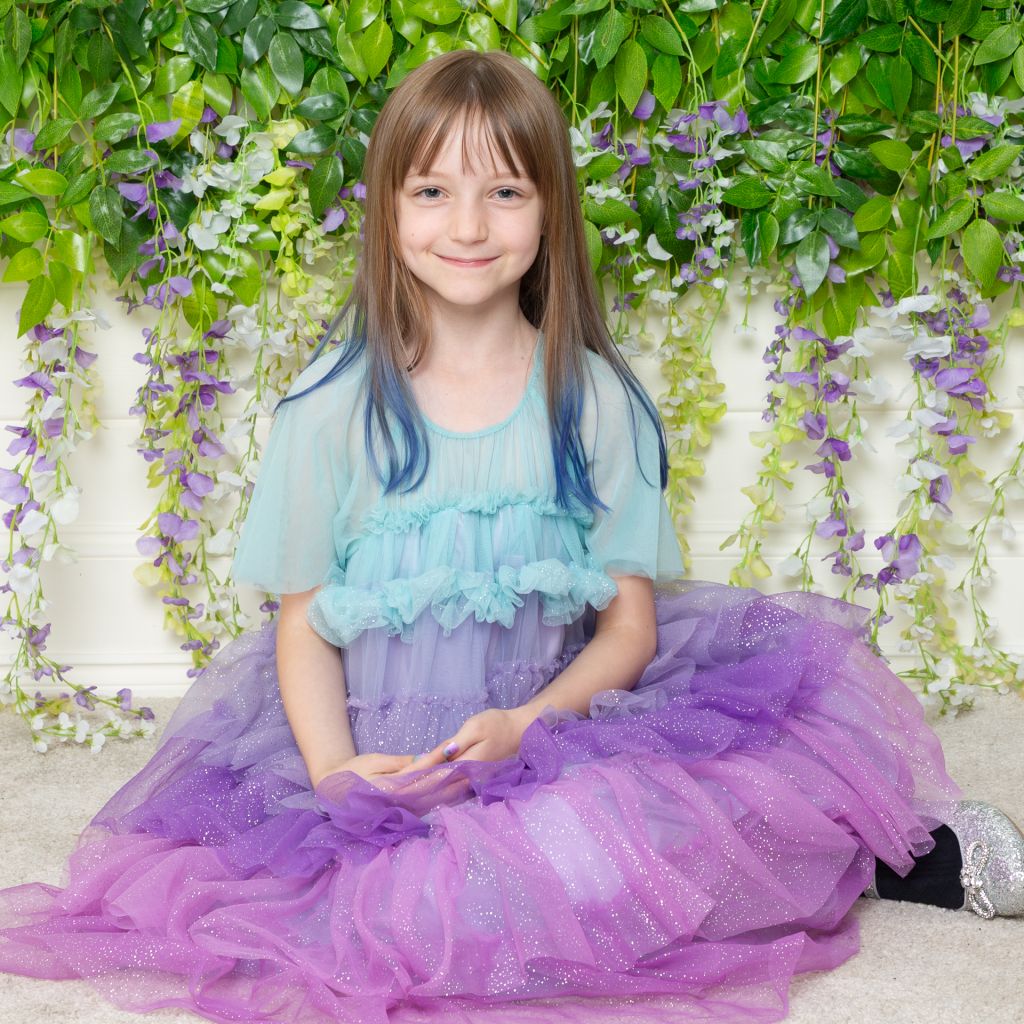 a little girl in purple sitting in front of a flower wall