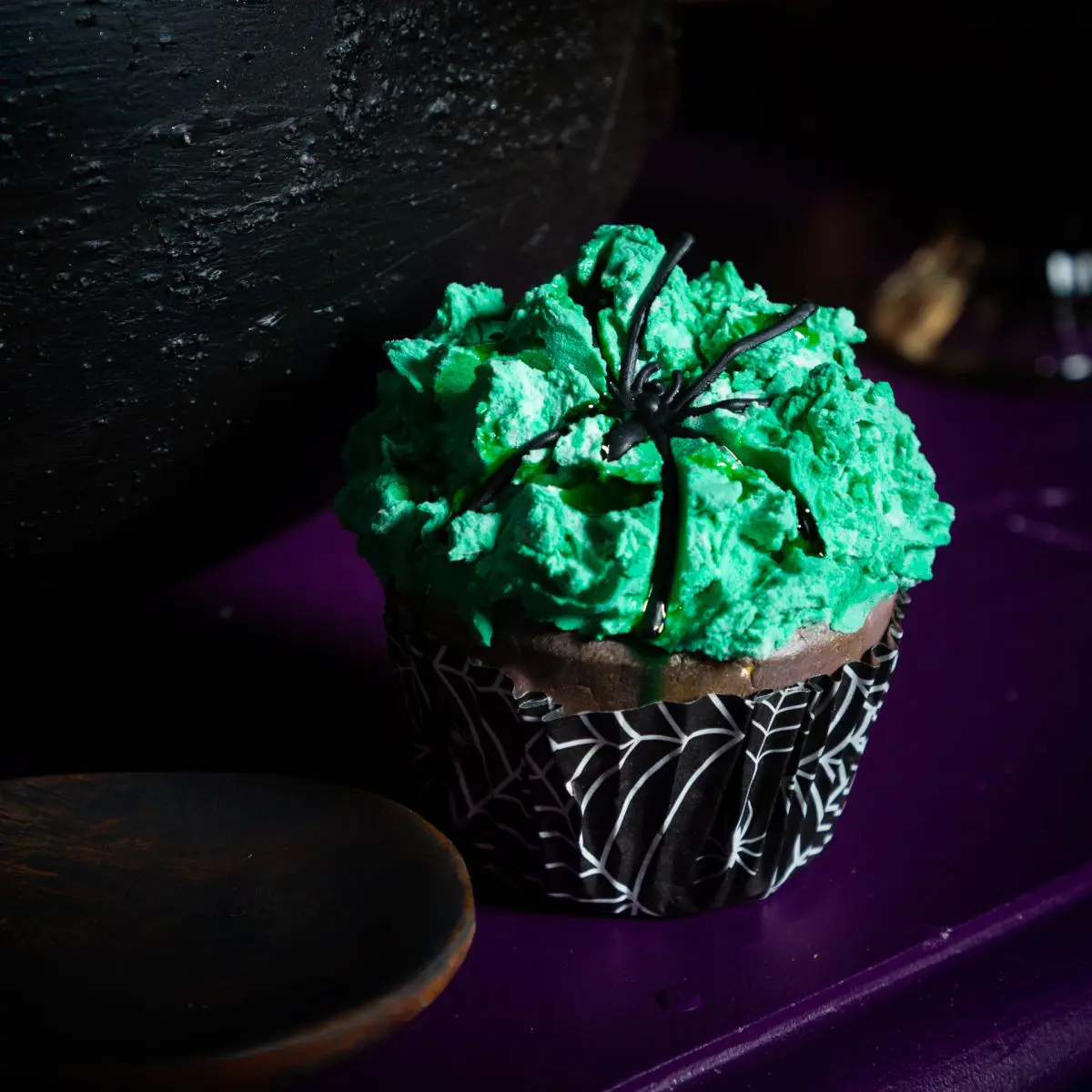 A cupcake with green icing and a spider decoration