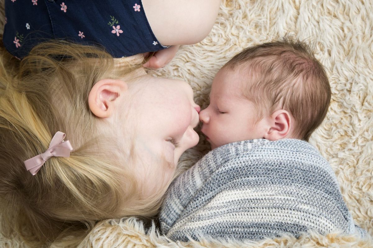a big sister kisses her newborn baby brother