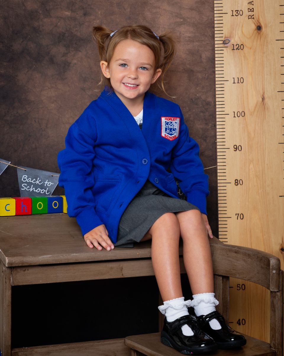 a little girl in a blue uniform sits on a school desk
