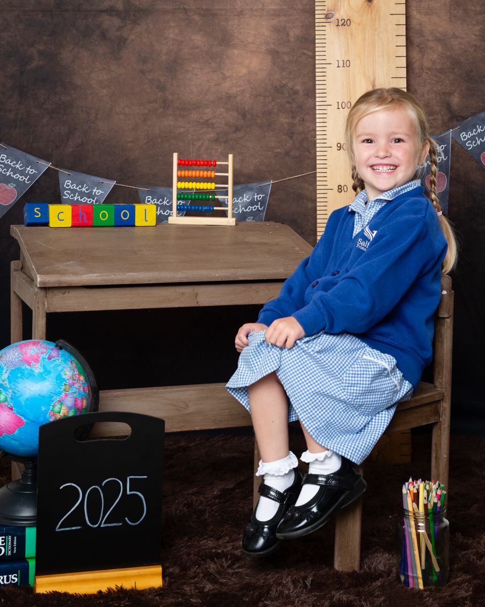 A little girl poses by a desk at a Starting School Photo shoot in West Sussex