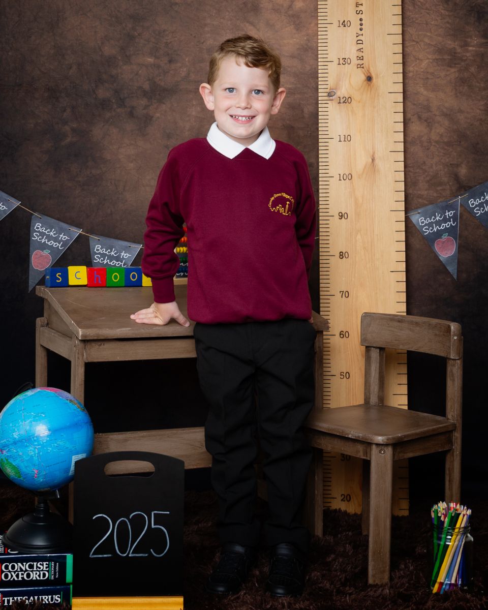 A little boy poses in a burgundy jumper desk at a Starting School Photo shoot in West Sussex