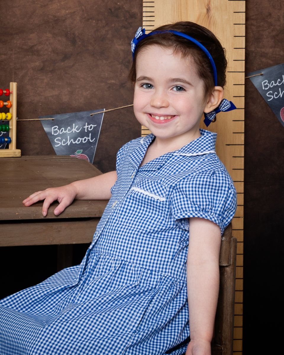 A little girl poses in a blue and white uniform at a Starting School Photo shoot in West Sussex