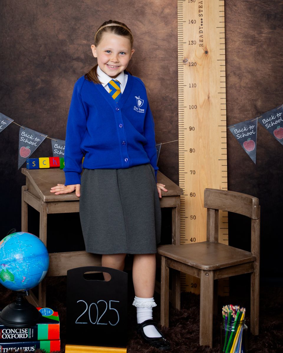A little girl poses on a desk at a Starting School Photo shoot in West Sussex