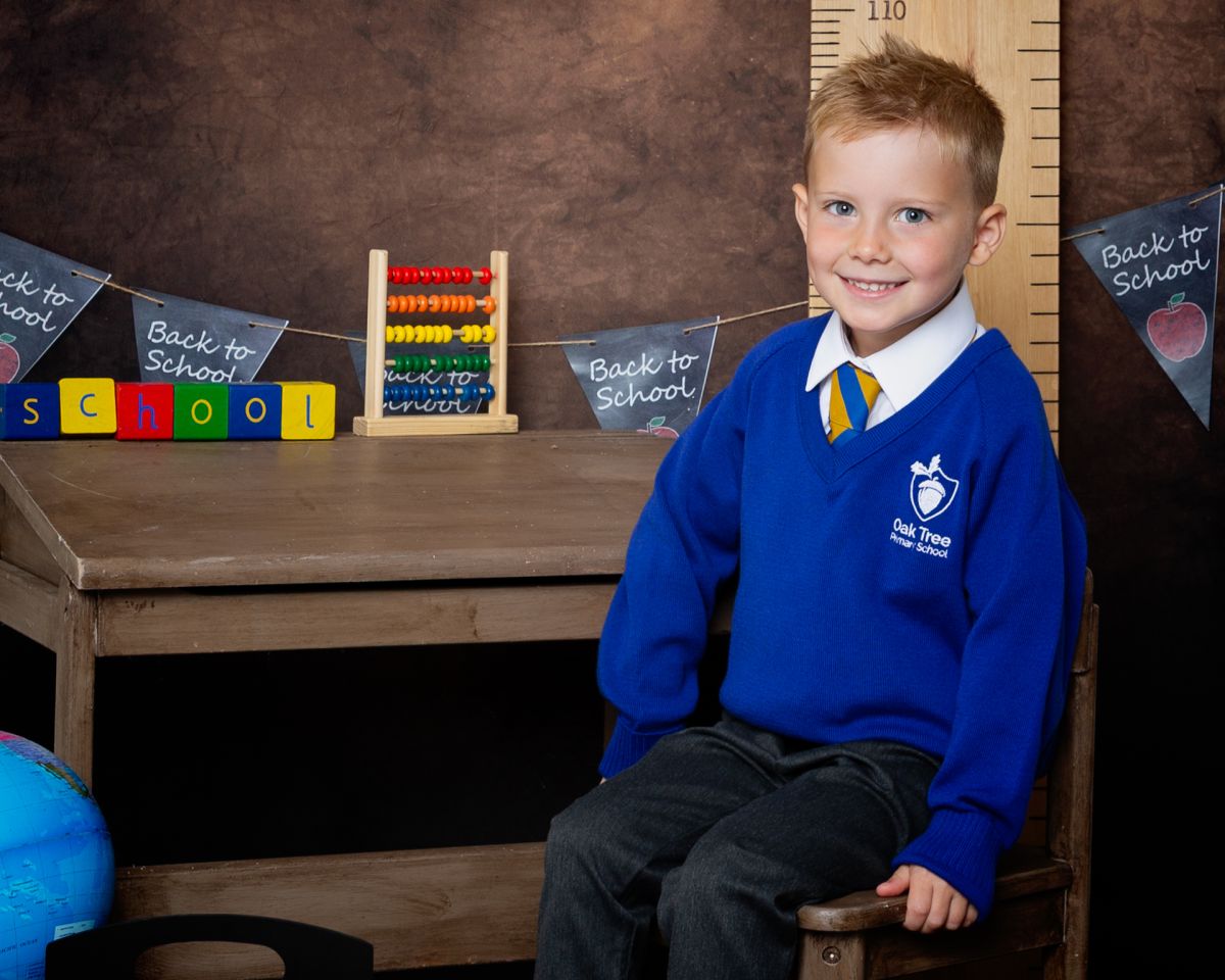 A little boy poses on a desk at a Starting School Photo shoot in West Sussex