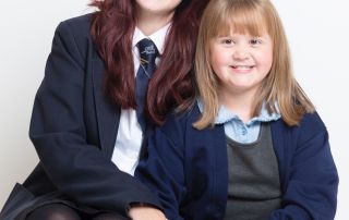 Two sisters from different schools in West Sussex pose together for school photos at a professional studio