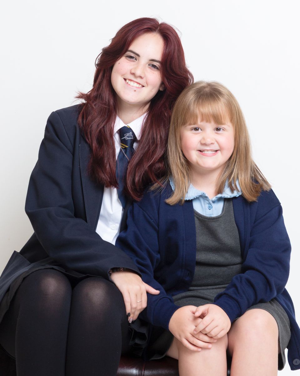 Two sisters from different schools in West Sussex pose together for school photos at a professional studio