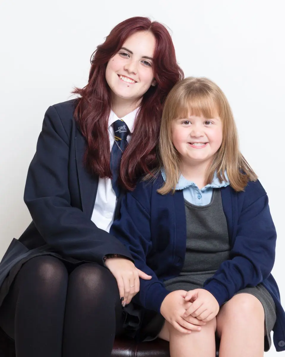 Two sisters from different schools in West Sussex pose together for school photos at a professional studio