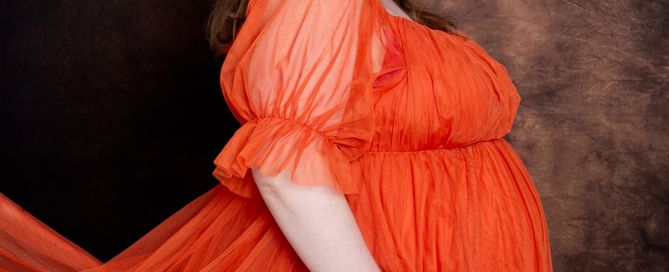 a pregnant woman poses in a bright orange dress with a floral crown