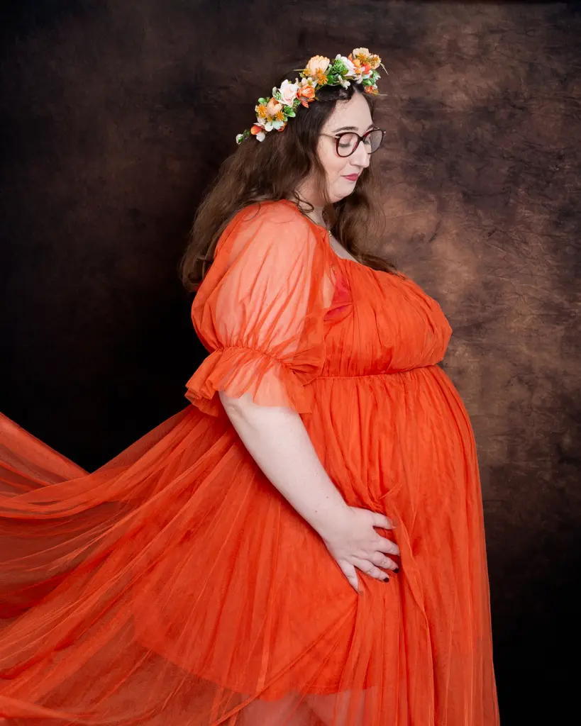 a pregnant woman poses in a bright orange dress with a floral crown