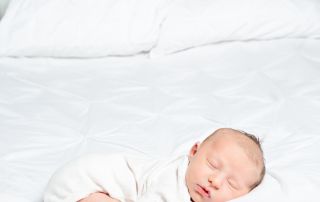 a baby in a white vest sleeps on a bed