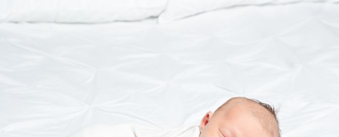 a baby in a white vest sleeps on a bed