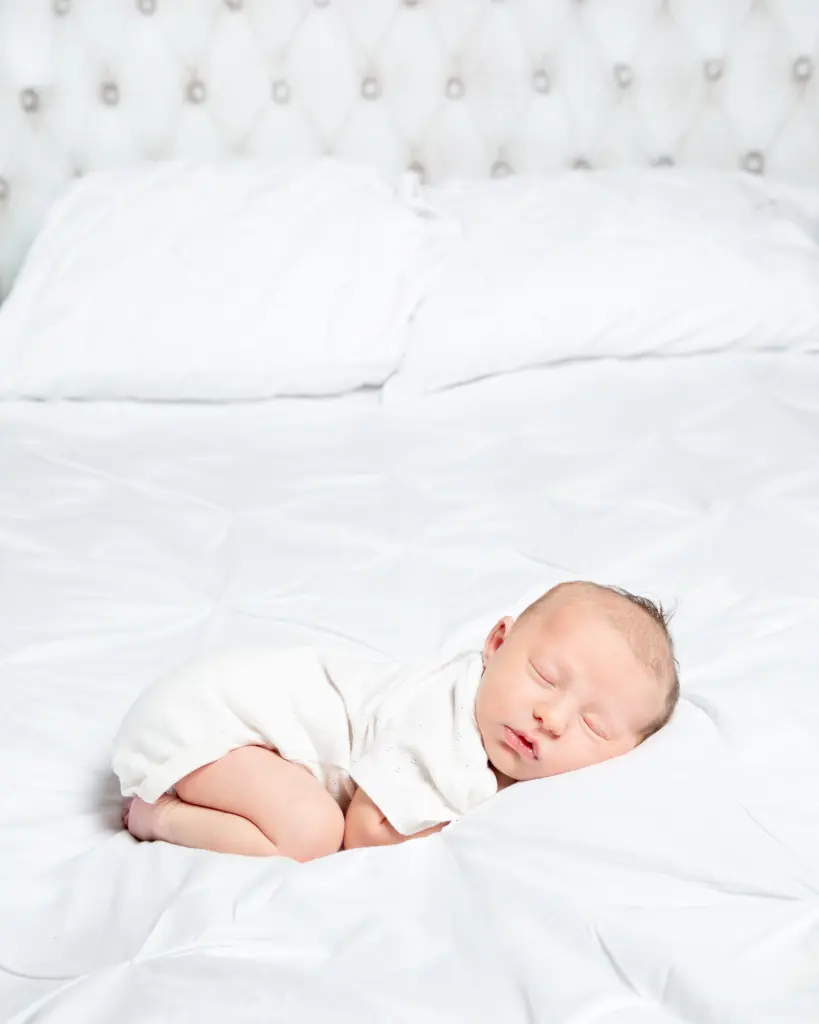 a baby in a white vest sleeps on a bed