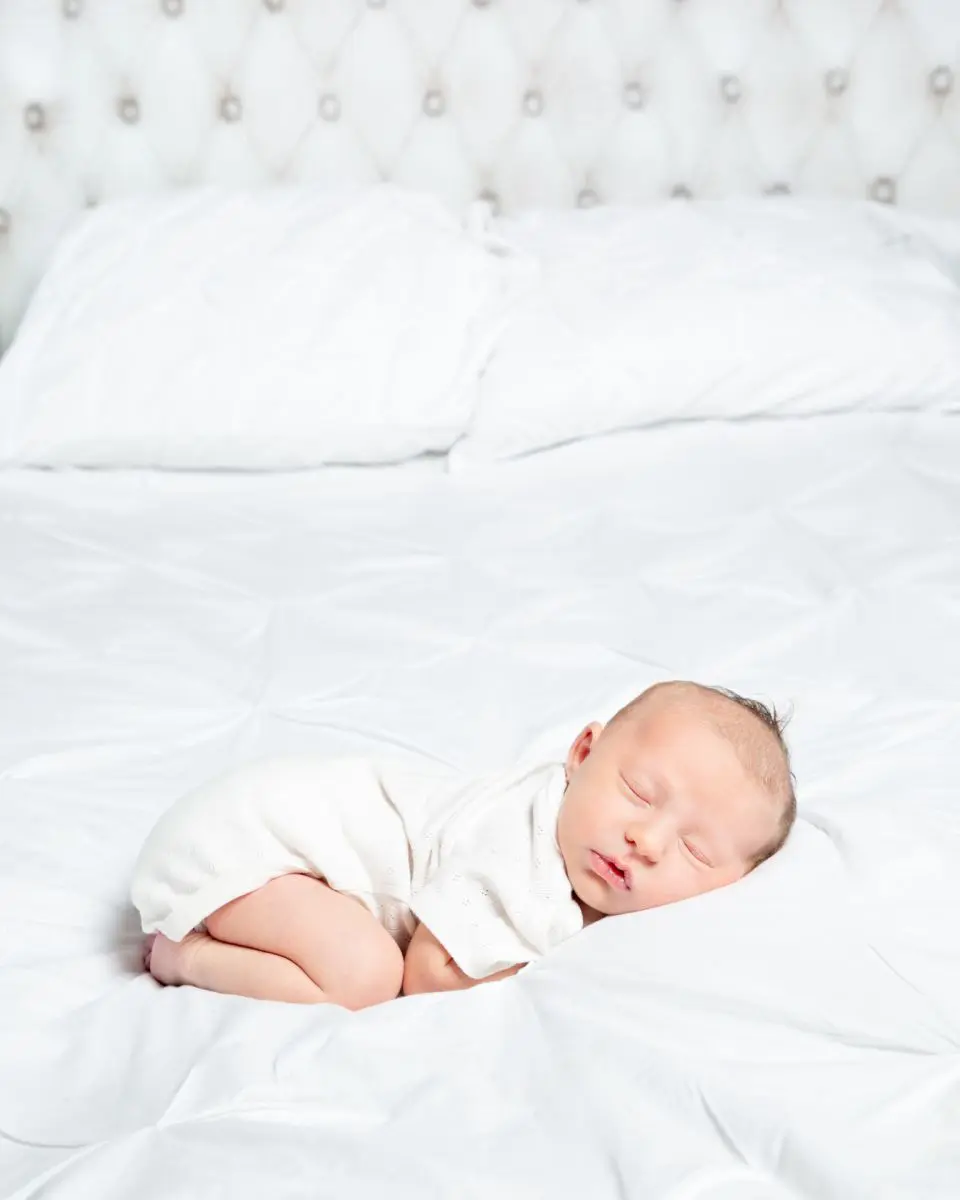 a baby in a white vest sleeps on a bed