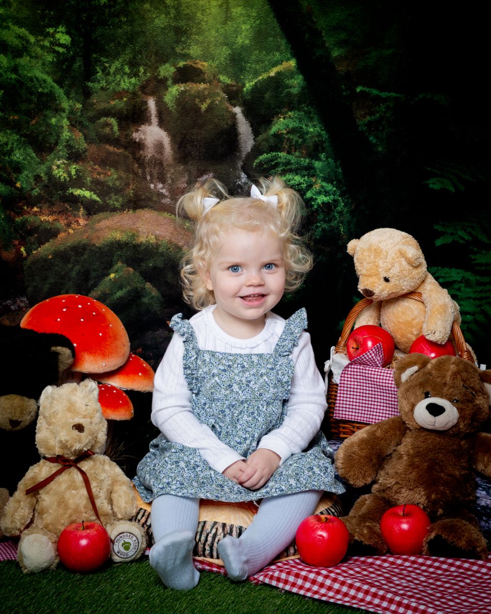 a little girl smiles in a teddy bears picnic themed set in the studio