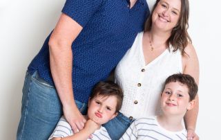 A family of mum dad and two boys pose together and one of the boys is pulling a funny face