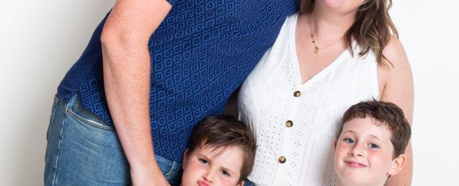 A family of mum dad and two boys pose together and one of the boys is pulling a funny face