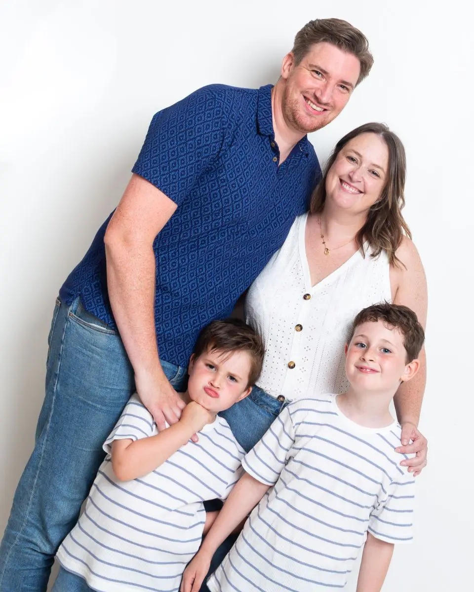 A family of mum dad and two boys pose together and one of the boys is pulling a funny face