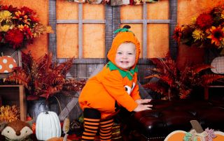 a little boy dressed as a pumpkin at a autumn themed photo shoot
