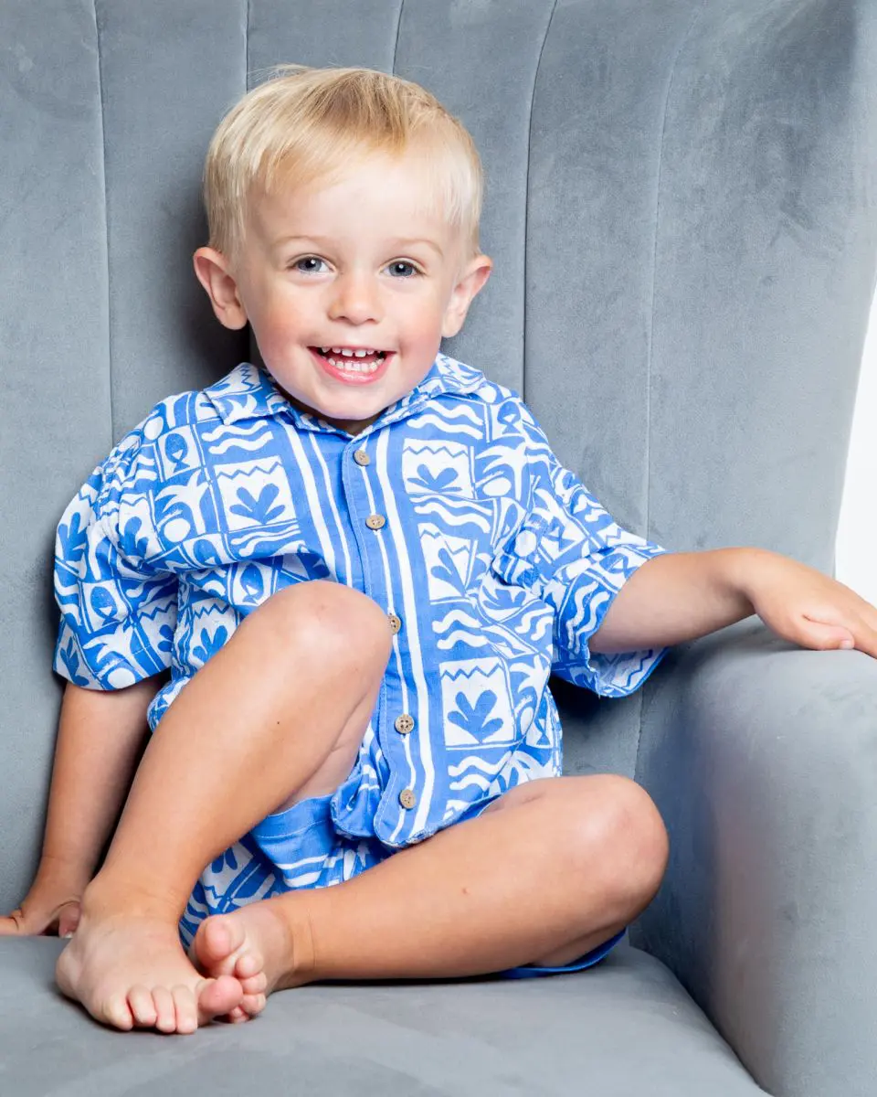 a little boy in a blue and white holiday outfit with a tan and blonde hair