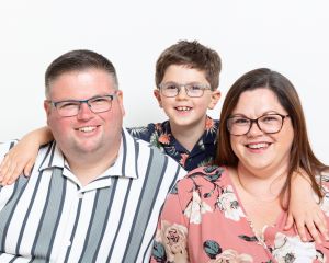 A family of mum, dad and son pose for the camera in a studio against a white background