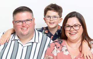 A family of mum, dad and son pose for the camera in a studio against a white background