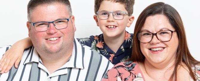 A family of mum, dad and son pose for the camera in a studio against a white background